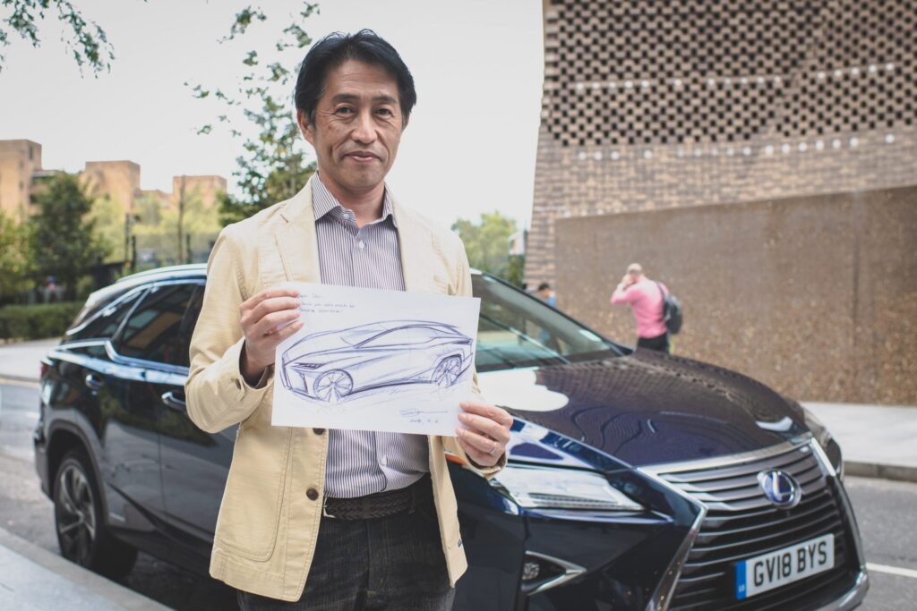 Automotive designer holding car sketch in front of a blue Lexus SUV on a city street