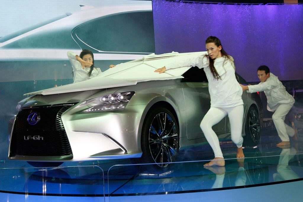 Silver Lexus LF-Gh concept car unveiled by dancers at auto show, dramatic lighting and reflective floor