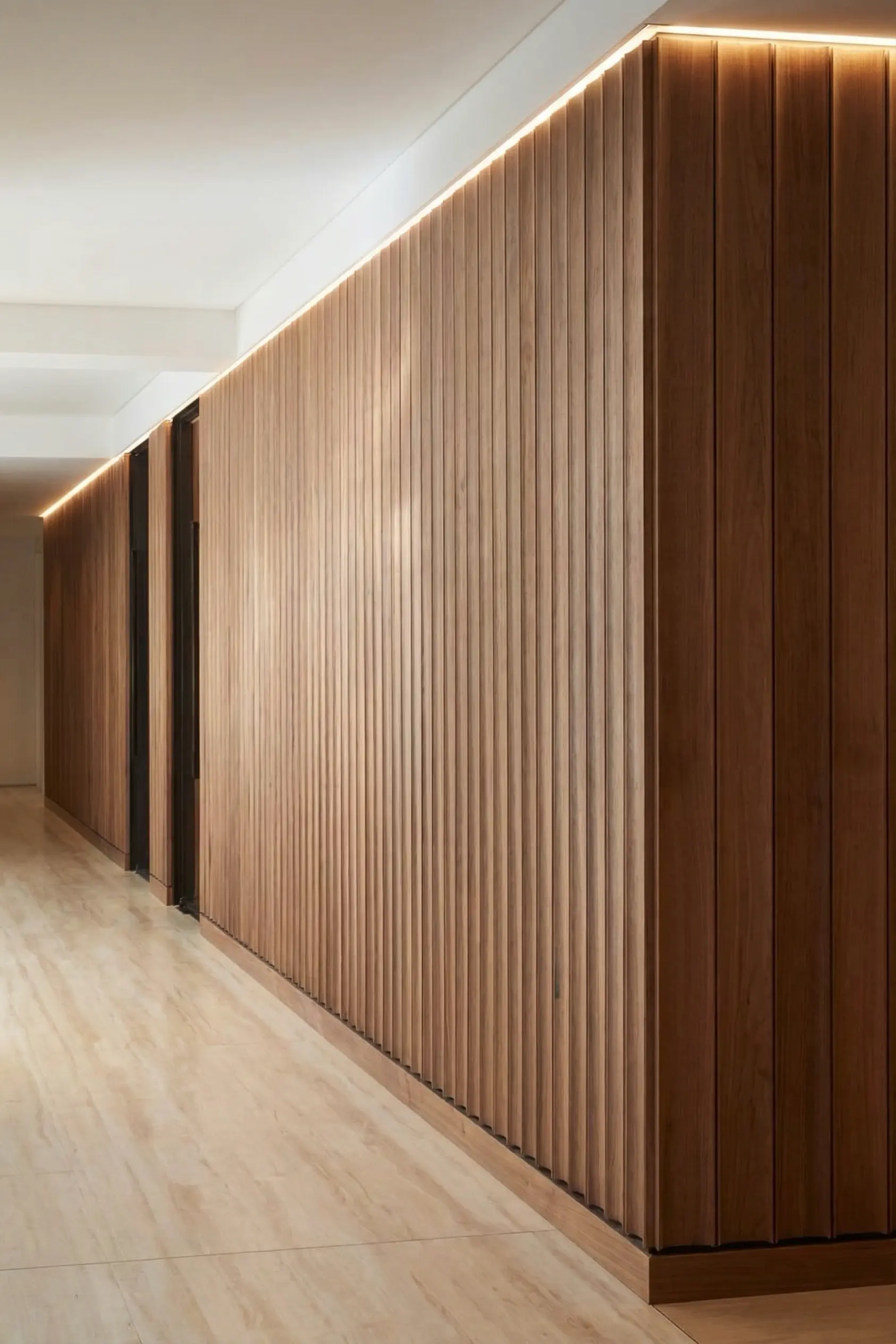 Minimalist hallway with vertical wooden slat feature wall, recessed LED strip lighting and light marble flooring