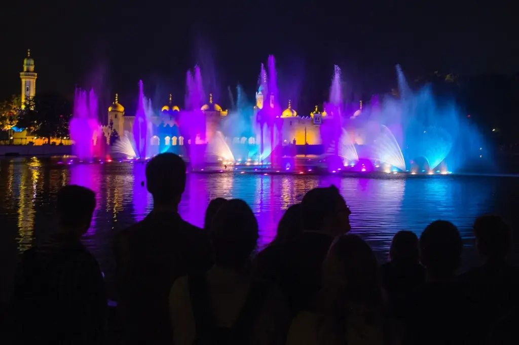 4 Silhouetted crowd watches colorful illuminated fountain show over lake at night with purple, blue and gold lights. | Sky Rye Design Silhouetted crowd watches colorful illuminated fountain show over lake at night with purple, blue and gold lights.