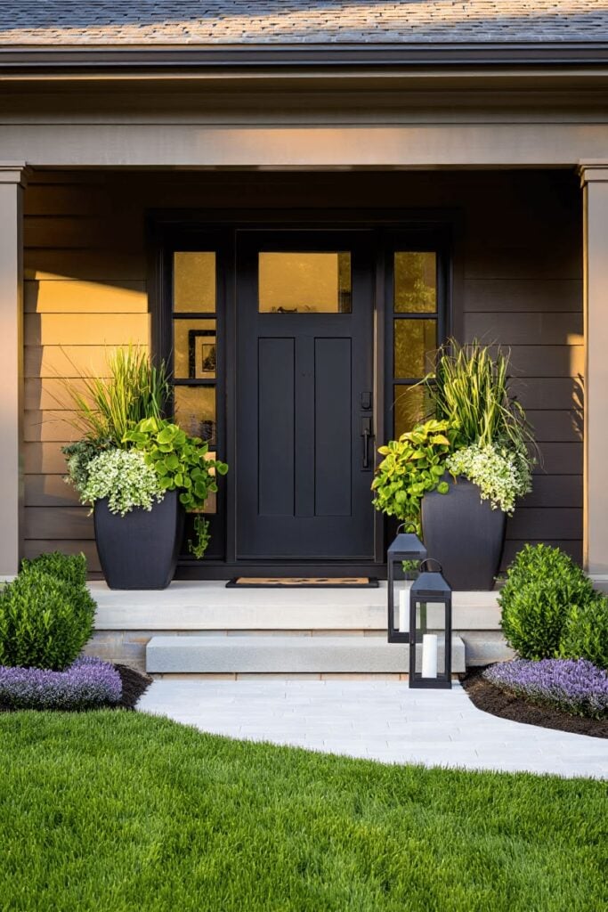 Modern black front door flanked by tall planters and lanterns on a landscaped porch, boosting curb appeal