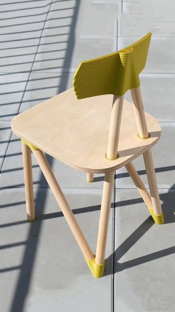 Modern minimalist wooden chair with yellow accents on sunlit tiled patio, sculpted backrest and angled legs