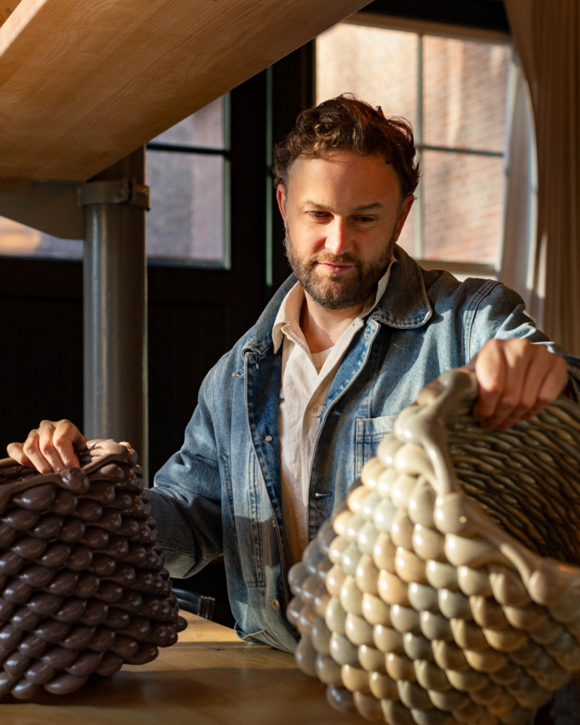 Ceramic artist in denim jacket examines large textured pottery vessels in sunlit studio, showcasing handmade decorative ceramics