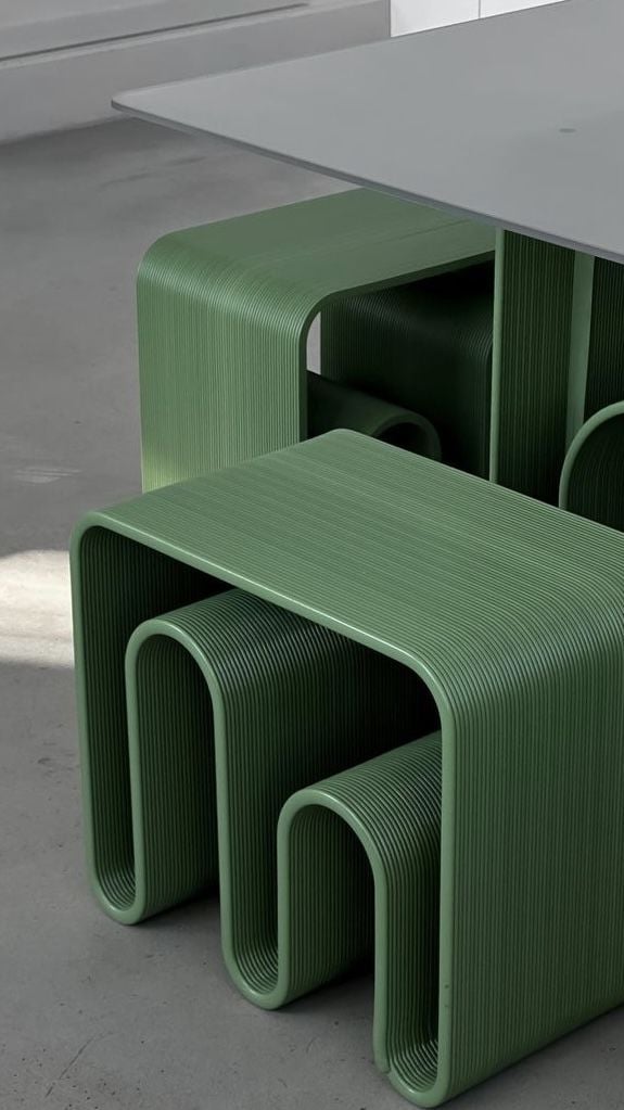 Green ribbed modern nesting stools under a white table on concrete floor, contemporary modular seating