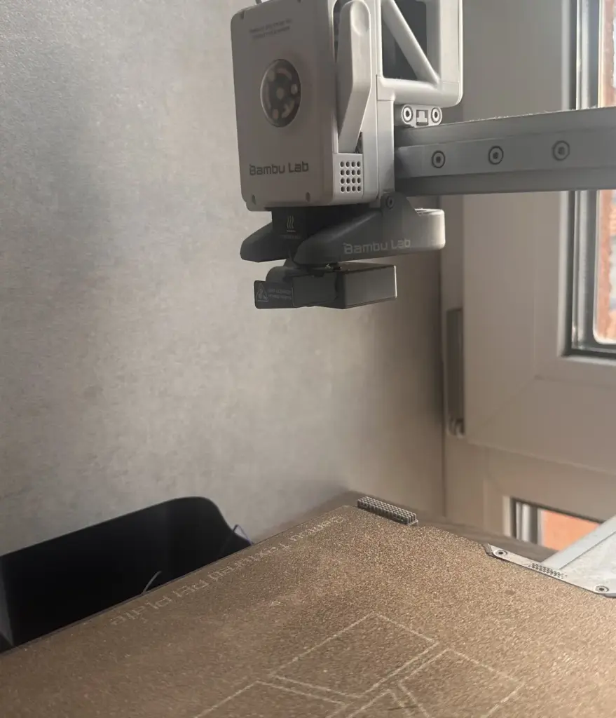 Bambu Lab 3D printer extruder and nozzle over textured build plate, 3D printing head near window