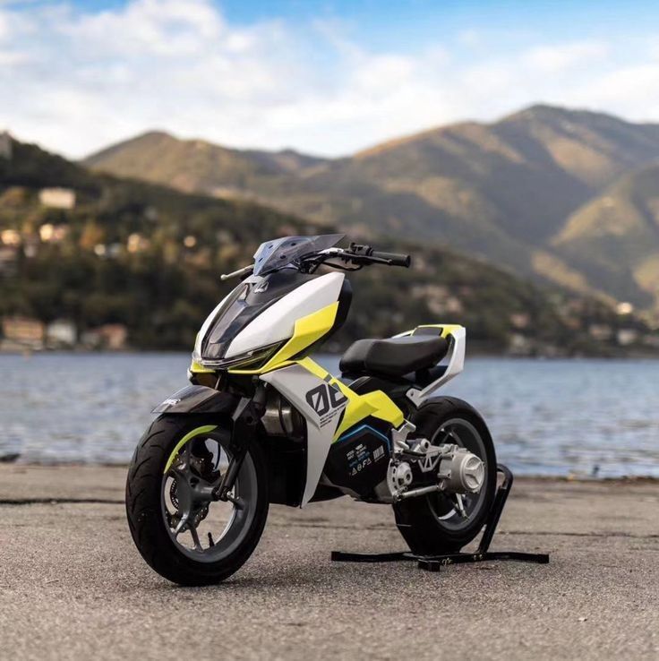 Sporty yellow-white electric motorcycle parked by a lake with mountains in background — modern urban electric bike design
