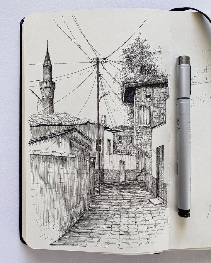 Black ink sketch in sketchbook of a narrow cobblestone street with old buildings, minaret, power lines and a pen.