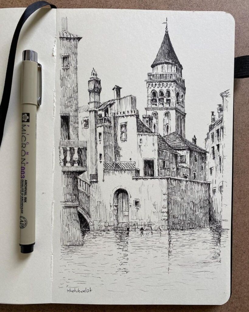 Pen-and-ink sketch in a sketchbook of historic waterfront buildings and a tower with reflections, Micron pen beside it