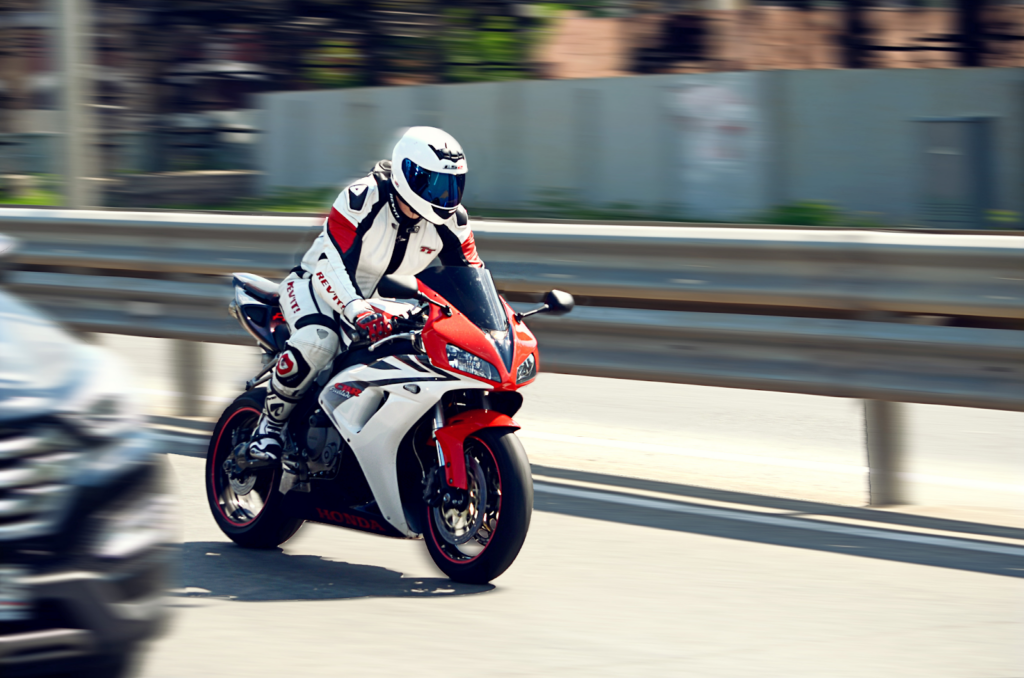 image Sportbike rider in white-red leathers and helmet on a red-and-white Honda motorcycle speeding past guardrail on road | Sky Rye Design Sportbike rider in white-red leathers and helmet on a red-and-white Honda motorcycle speeding past guardrail on road