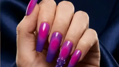 Close-up of long glossy pink-to-purple ombre coffin-shaped acrylic nail art with water droplets on dark satin background