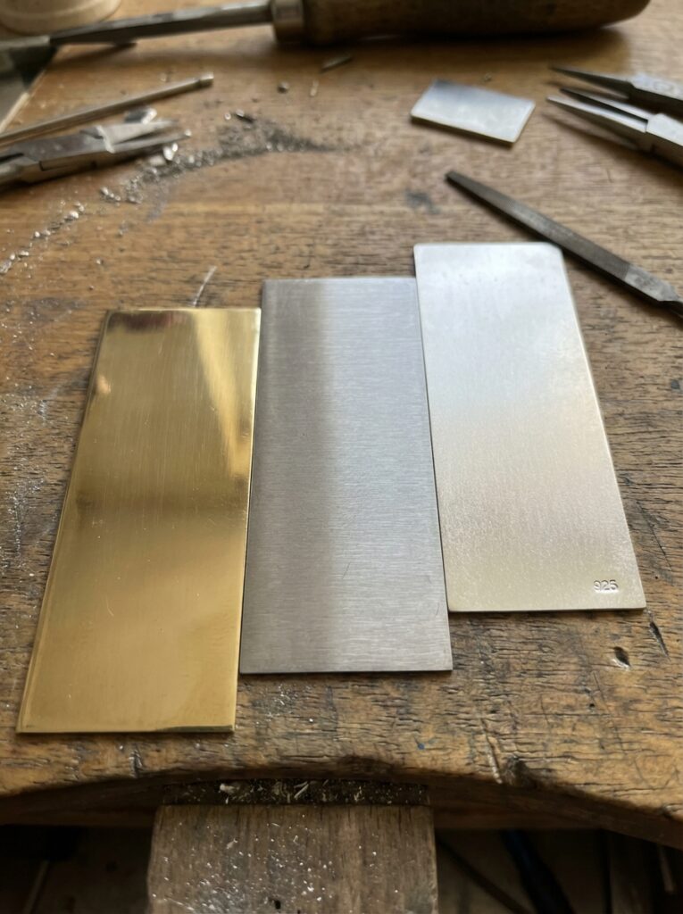 Brass and silver metal sheets (one stamped 925) on a jeweler's workbench with files and pliers