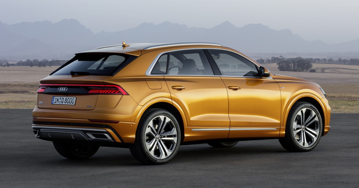 Golden Audi Q8 SUV rear three-quarter view parked on road with distant mountains, modern luxury crossover