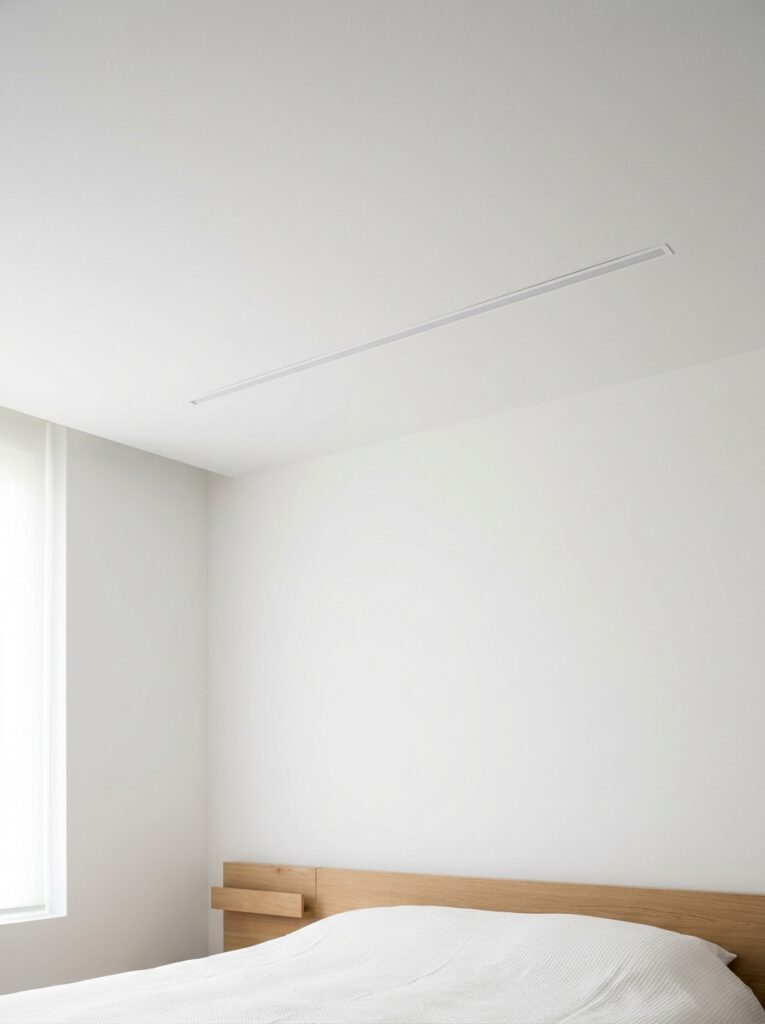 Minimal modern bedroom interior with white walls, wooden headboard, recessed ceiling light and natural window light.