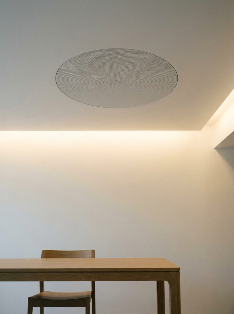 Minimal dining room with wooden table and chair under cove lighting and round perforated ceiling speaker