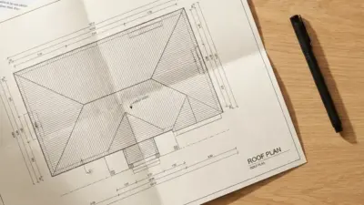 Architectural roof plan blueprint on wooden desk with black pen, top-view house roof layout and measurements