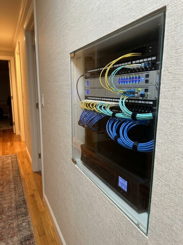 Recessed home network rack with patch panels and neatly bundled blue, yellow and green Ethernet and fiber cables