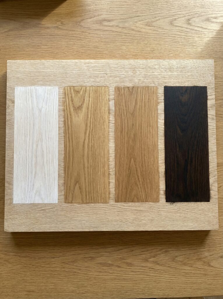 Four oak flooring swatches (whitewashed, light, natural, dark) displayed on an oak sample board
