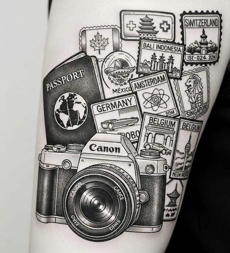 Black and gray travel-themed tattoo of a Canon camera, passport and country stamps (Belgium, Germany, Bali, Singapore)
