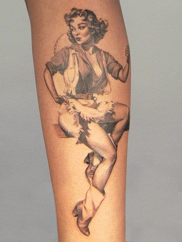 Black-and-gray vintage pin-up cowgirl tattoo on forearm, seated with boots, vest and short fringe skirt