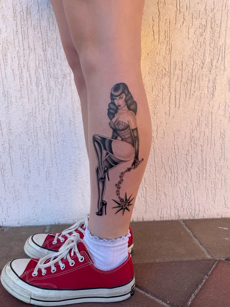 Calf tattoo: blackwork pinup woman in stockings holding a spiked mace, shown with red sneakers and white socks