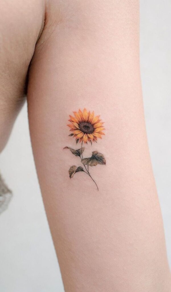 Small sunflower tattoo in fine-line color with thin stem and leaves on inner forearm, minimalist floral body art