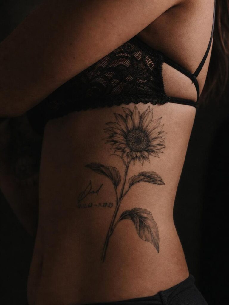 Sunflower rib tattoo — memorial Dad with dates — side tattoo shown beneath black lace bralette