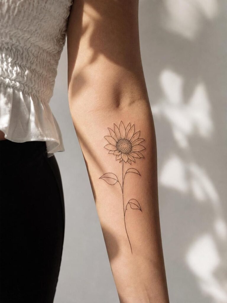 Delicate minimalist black-line sunflower tattoo on inner forearm, single-stem floral forearm ink.