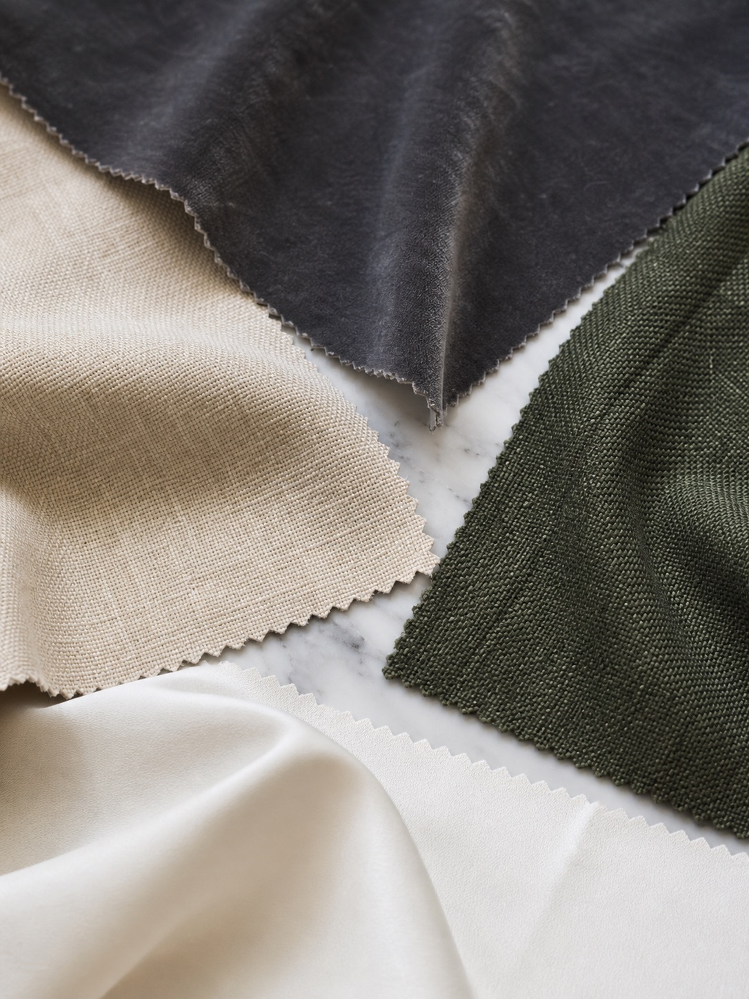 Close-up of charcoal, sand, forest green, and ivory blackout curtain fabric swatches on marble.