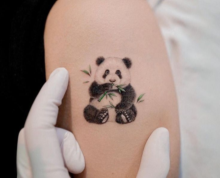 Small black-and-white panda tattoo on upper arm holding bamboo, cute minimalist design