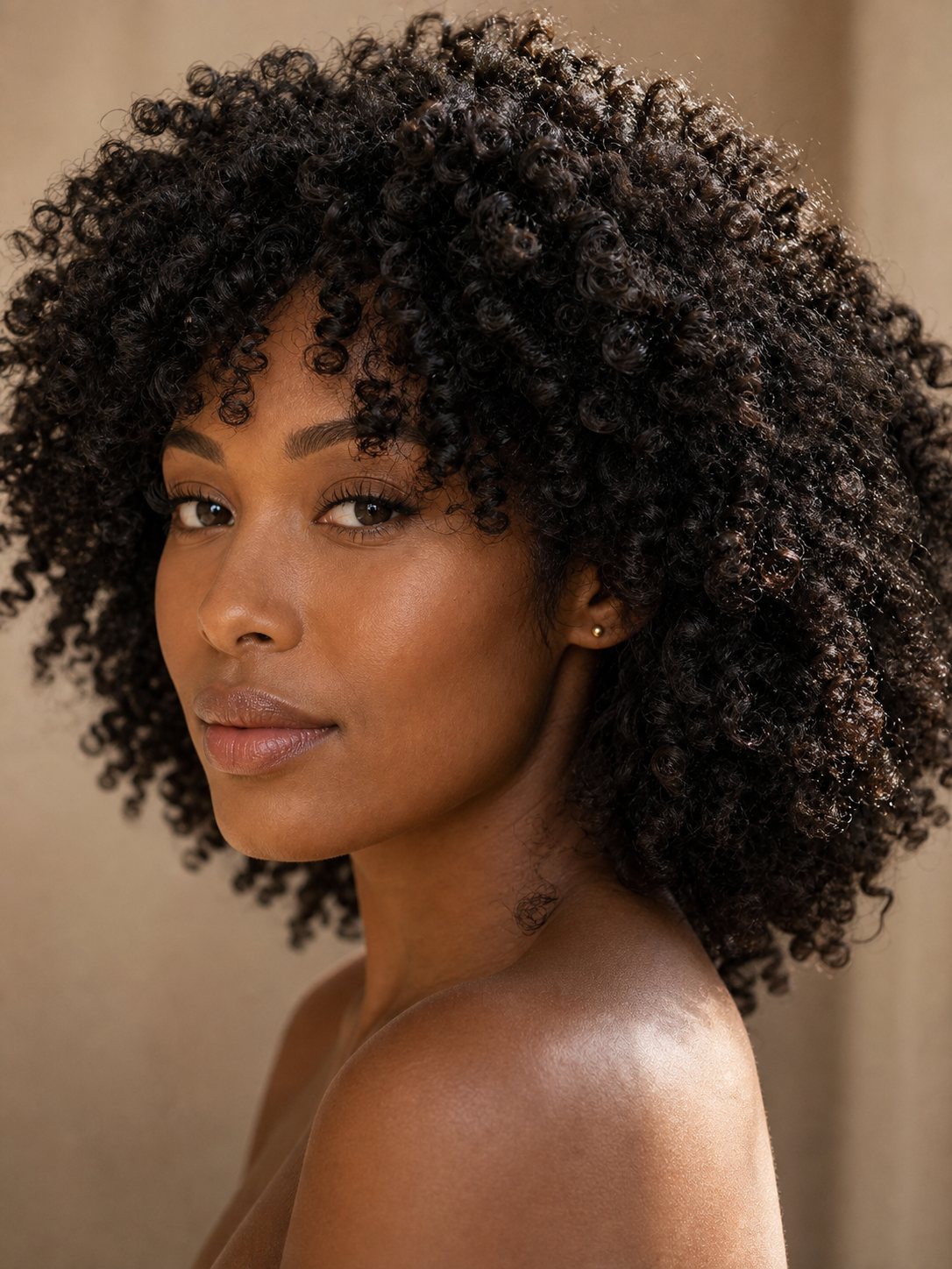 Close-up portrait of a Black woman with a defined kinky curly wig and tight coil texture.