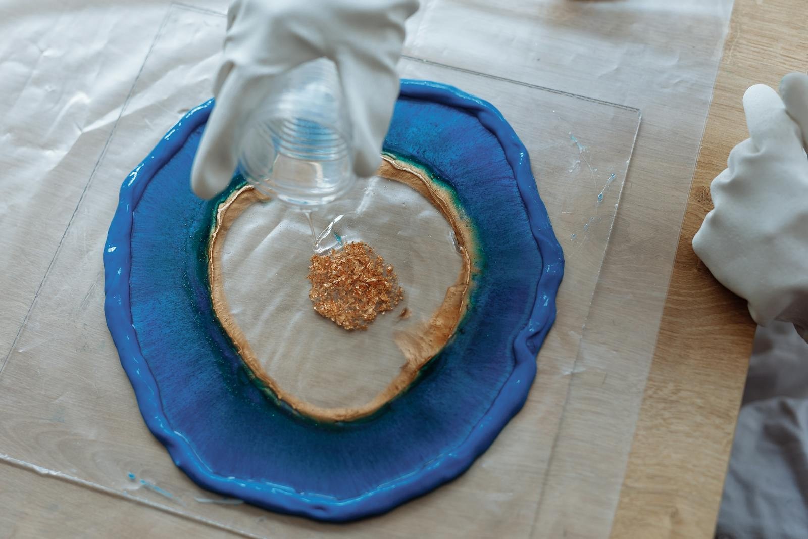 Landscape photo of resin art being poured with blue pigment and glitter on a work surface.