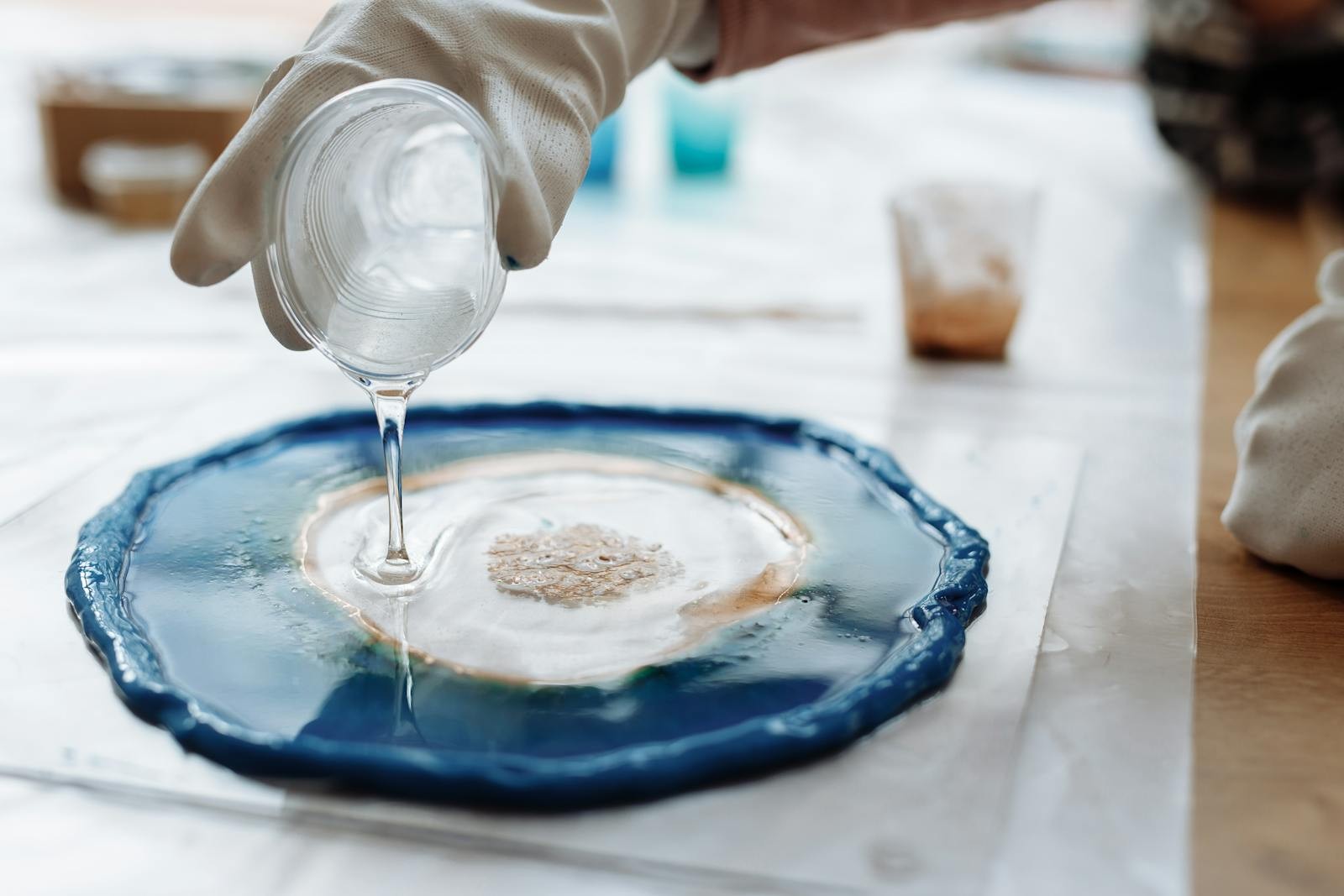 Landscape detail photo of gloved hands working with resin art materials and a mixing cup.