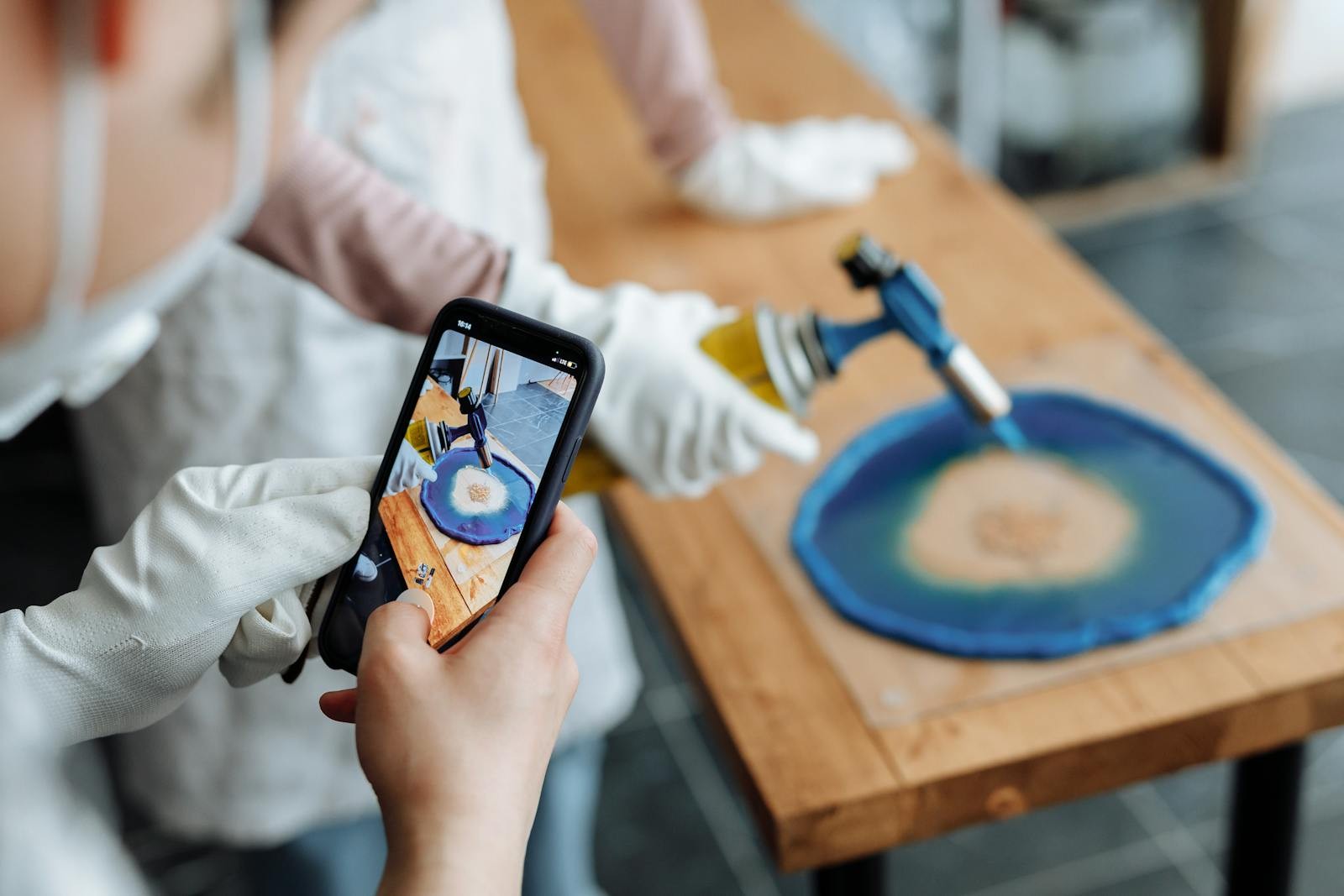 Landscape photo of a resin art process being filmed on a smartphone while a torch is used.