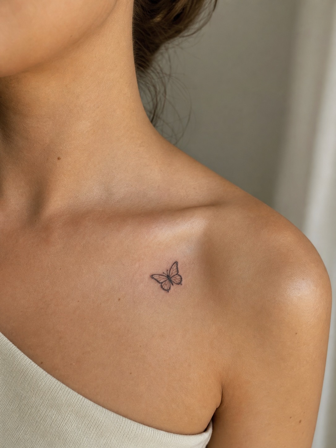 Small fine-line butterfly tattoo near the collarbone.