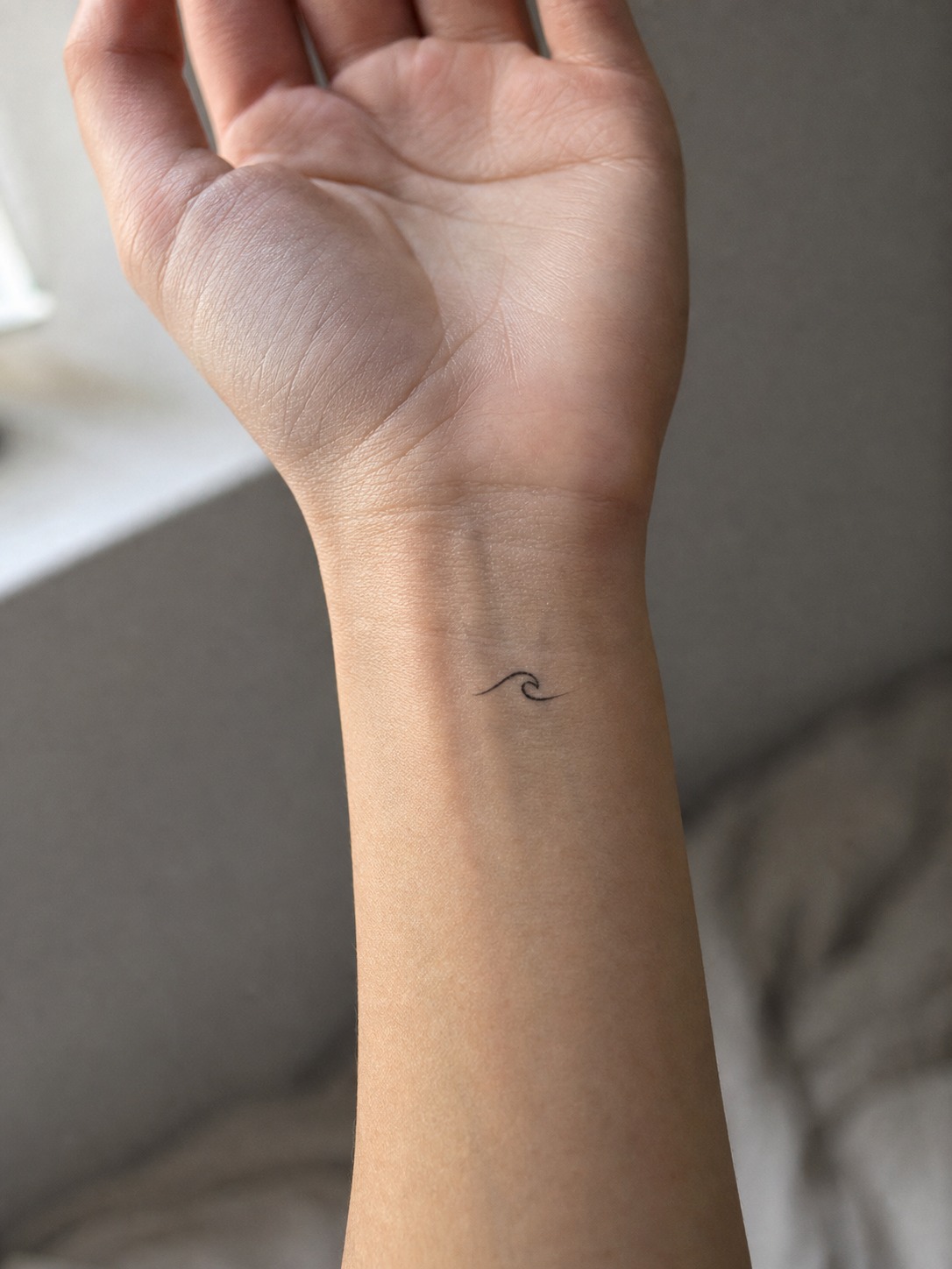 Tiny fine-line wave tattoo on the inner wrist in soft natural light.