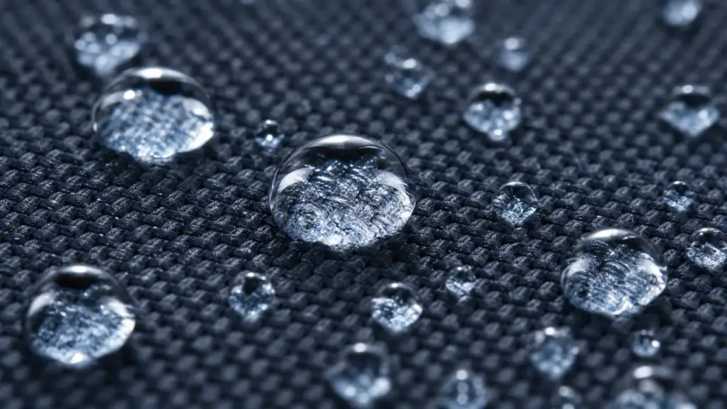 Water-repellent woven fabric close-up with beaded water droplets, hydrophobic textile texture