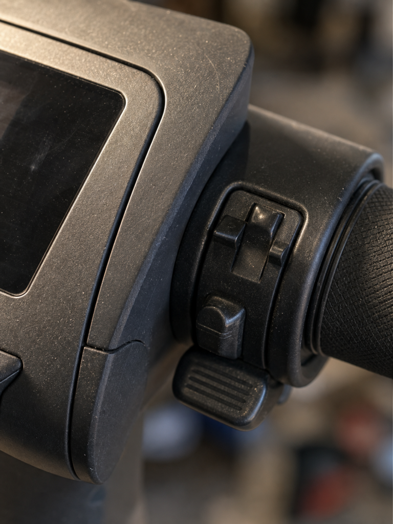 Electric scooter handlebar close-up showing throttle grip, toggle switches and control panel