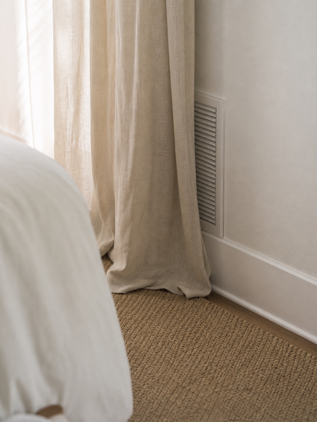 A wall return air grille partly covered by a long curtain panel.