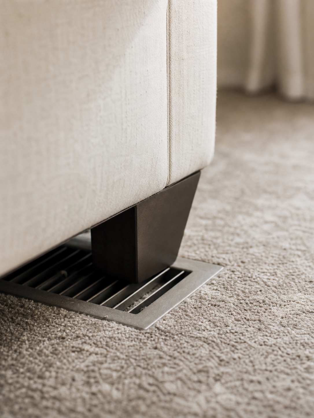 A floor AC supply vent partly blocked by an upholstered sofa leg.