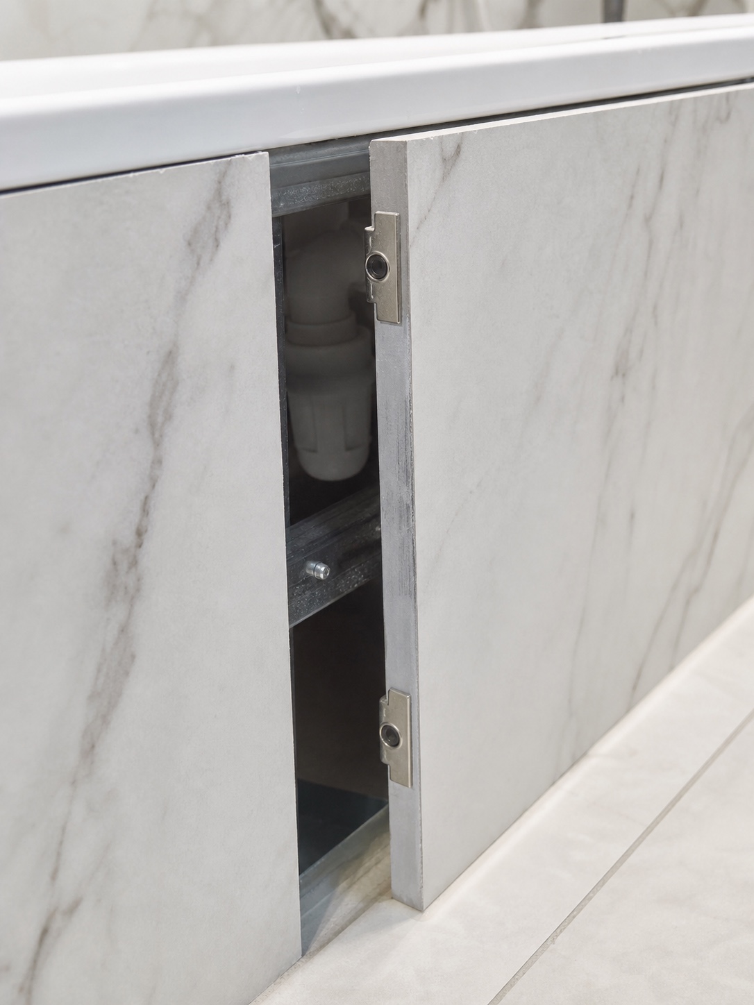 A removable tiled bath side panel opened slightly to show the concealed catch and plumbing access behind the marble-look tile.