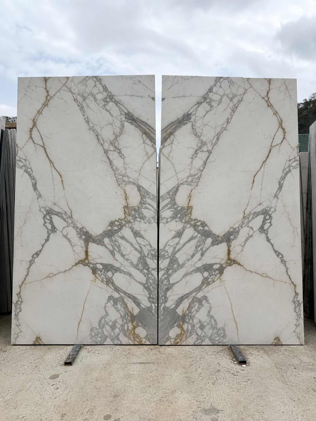 Two book-matched Calacatta marble slabs opened to show mirrored veining at a stone yard.