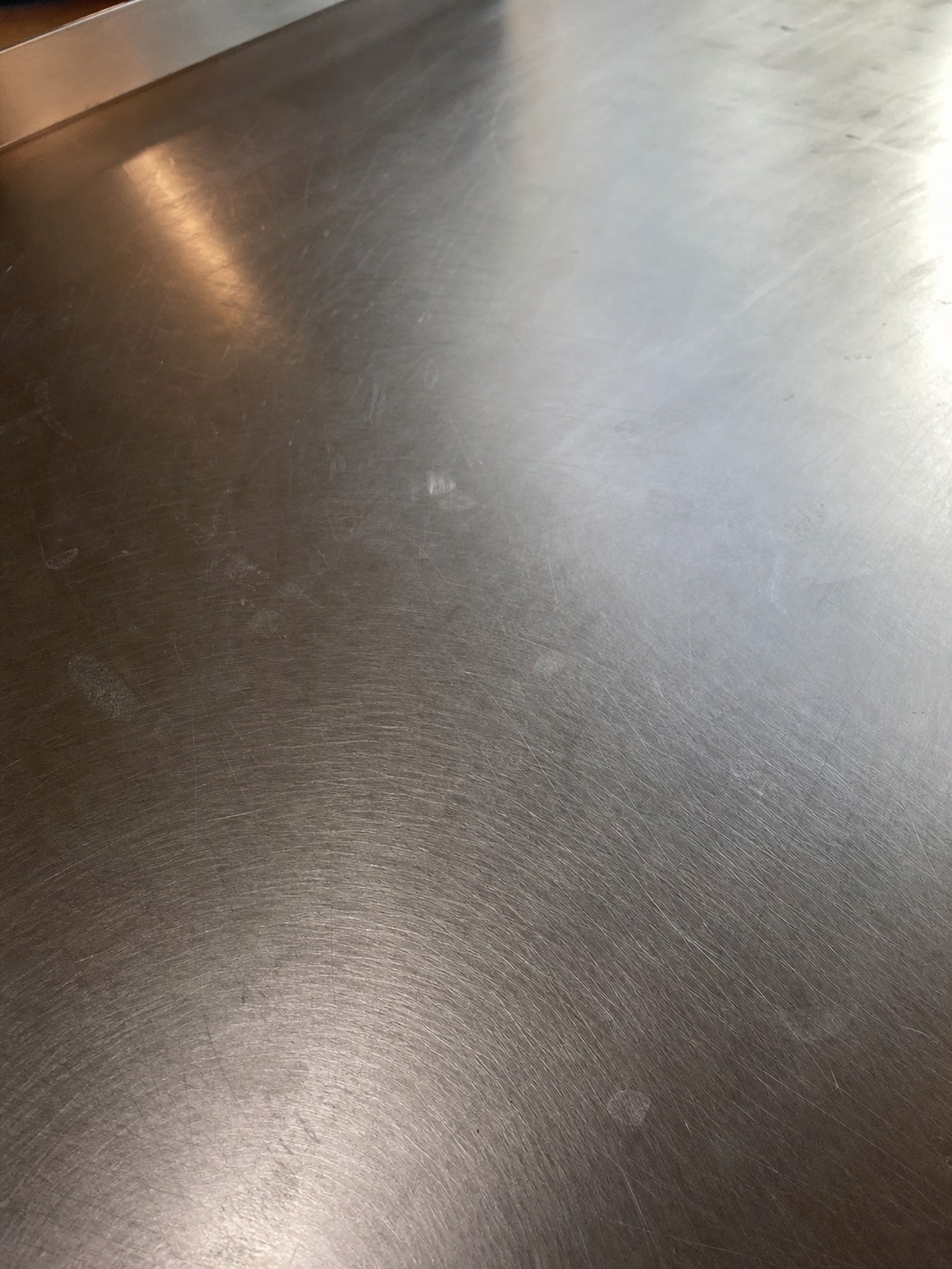 Close view of a brushed stainless steel prep counter with natural tool marks and light patina.