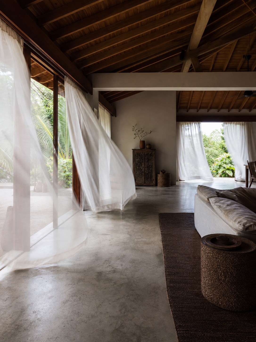 An airy living room with opposite openings and sheer curtains moving in a cross breeze.
