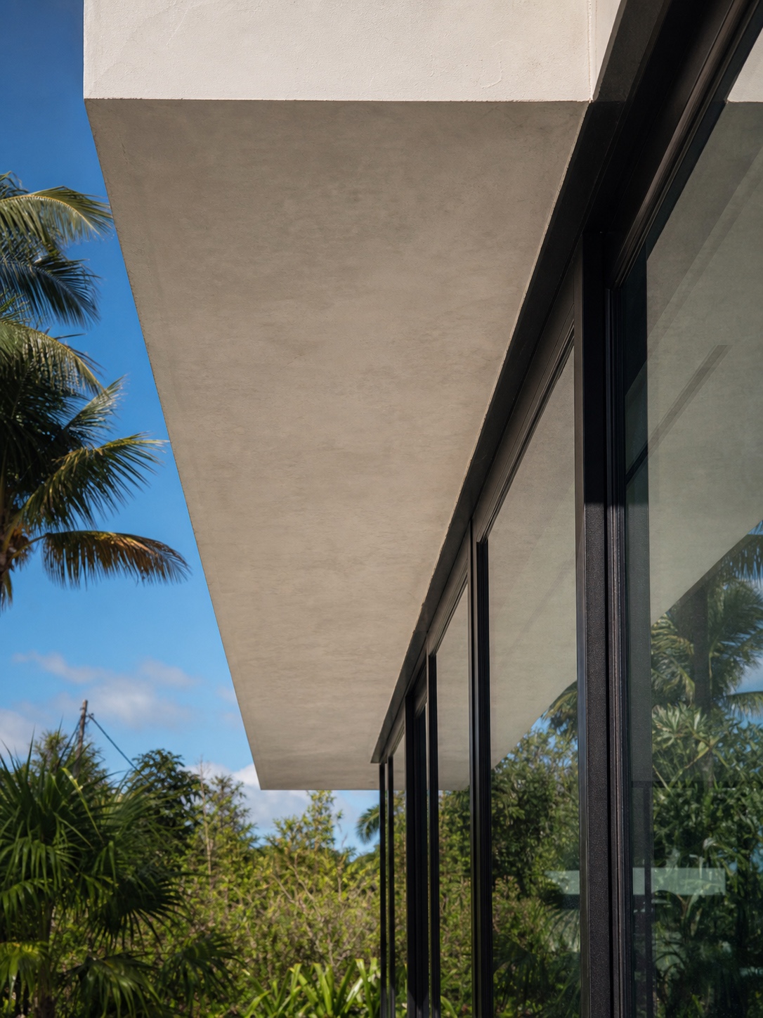 A close architectural detail of a flat concrete roof overhang casting shade across a black-framed glass wall.