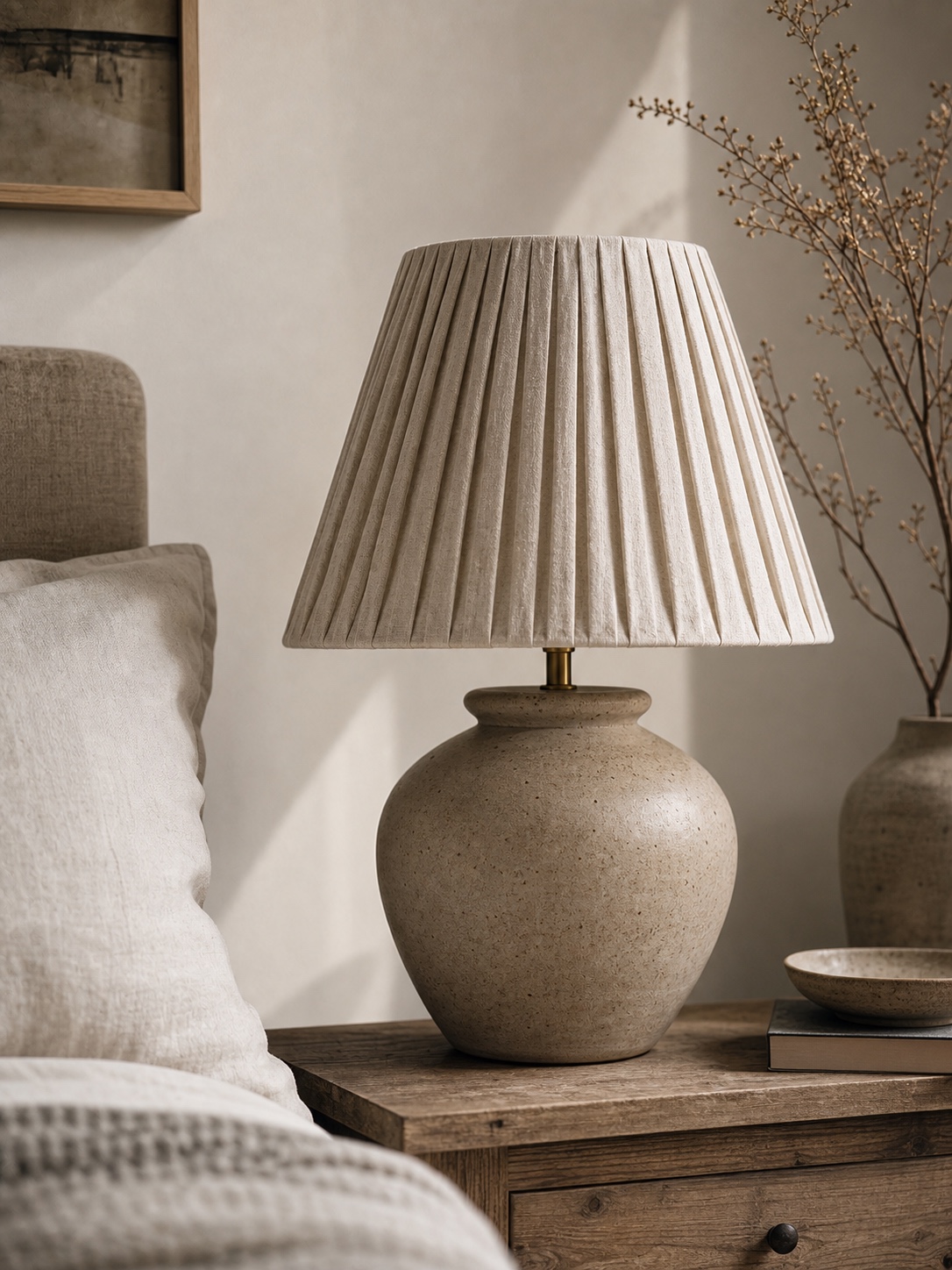 Pleated linen DIY lamp shade on a ceramic table lamp in a neutral bedroom setting.