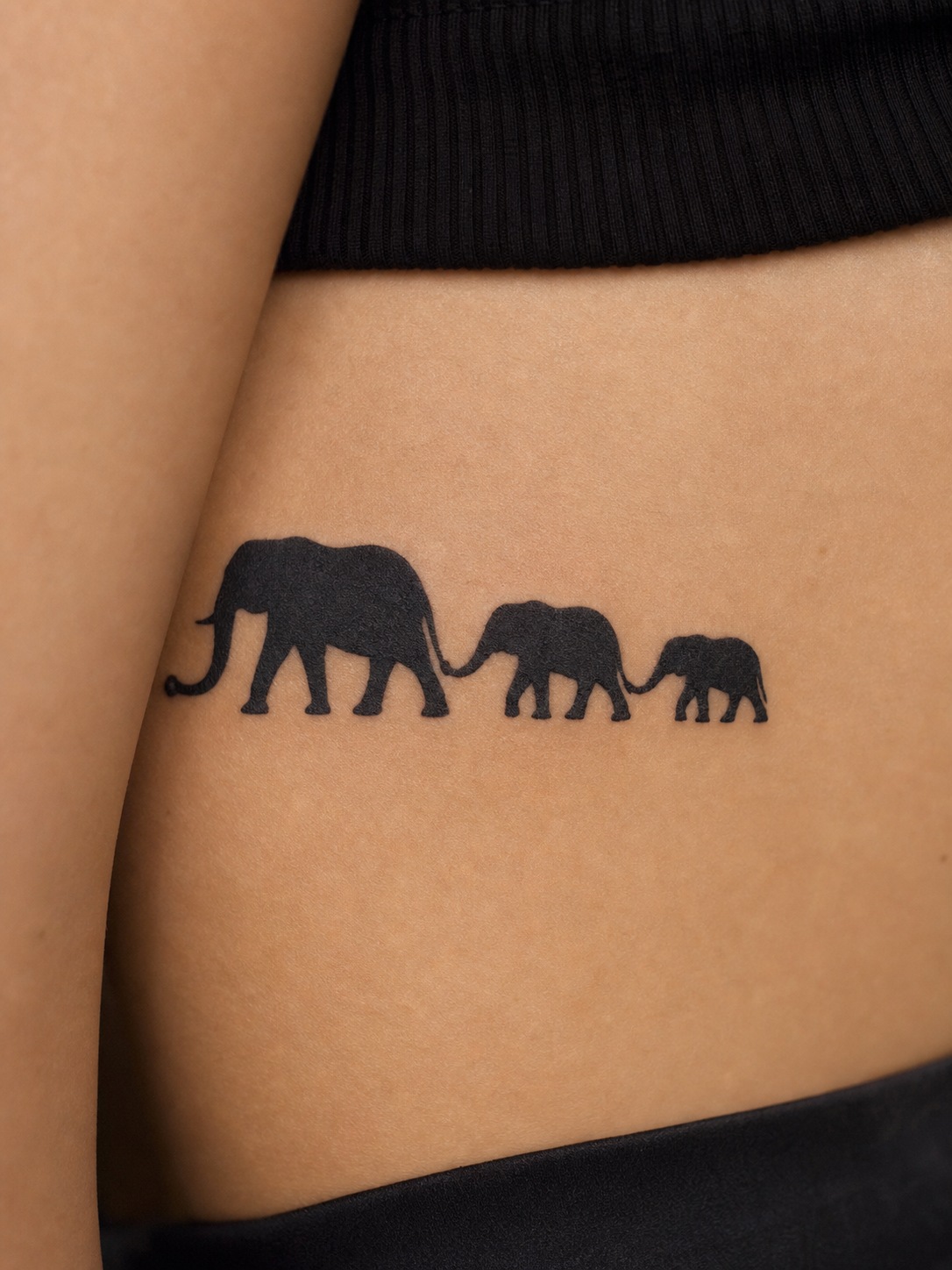 Horizontal elephant family silhouette tattoo with connected trunks.