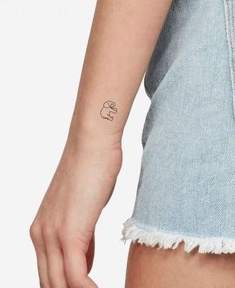 Minimalist small elephant outline wrist tattoo on person wearing frayed denim shorts