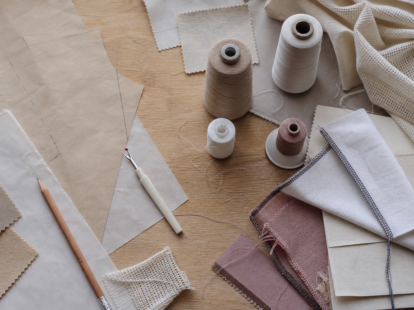 Flat lay of seam finishing tools, thread cones, pattern paper, and overlocked fabric offcuts.