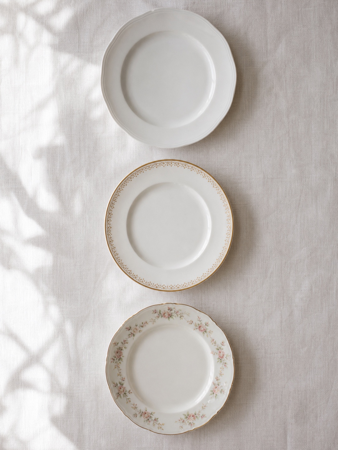 Three formal dinner plates on white linen showing plain porcelain, a gold rim, and a floral border.