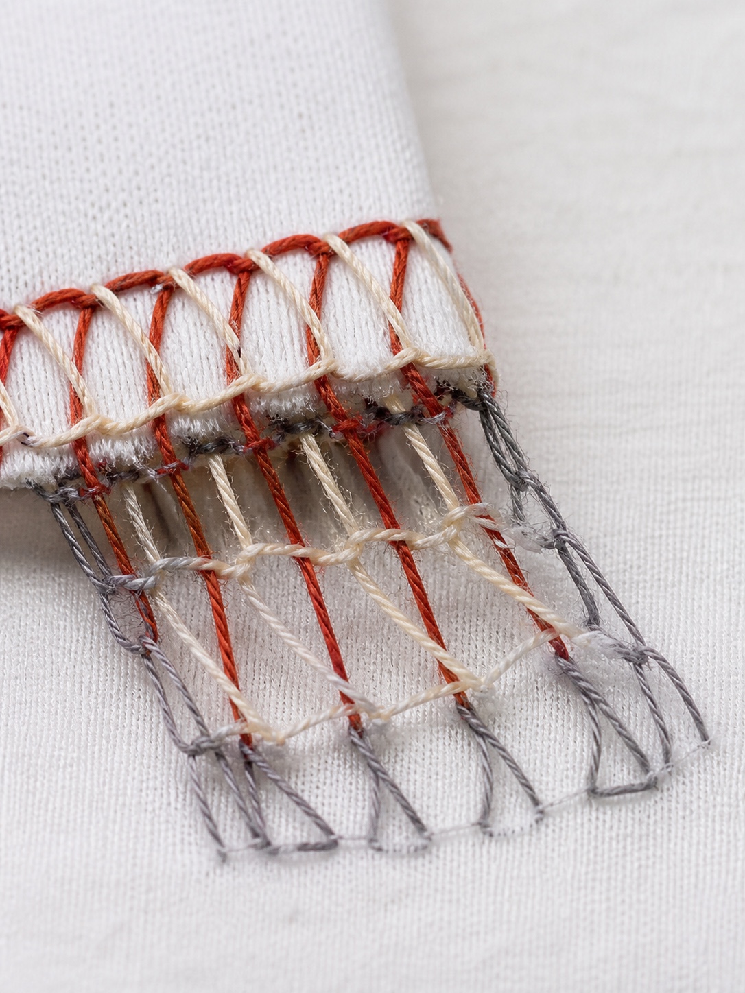 Close macro detail of a four-thread overlock seam with cream, rust, and gray thread paths.